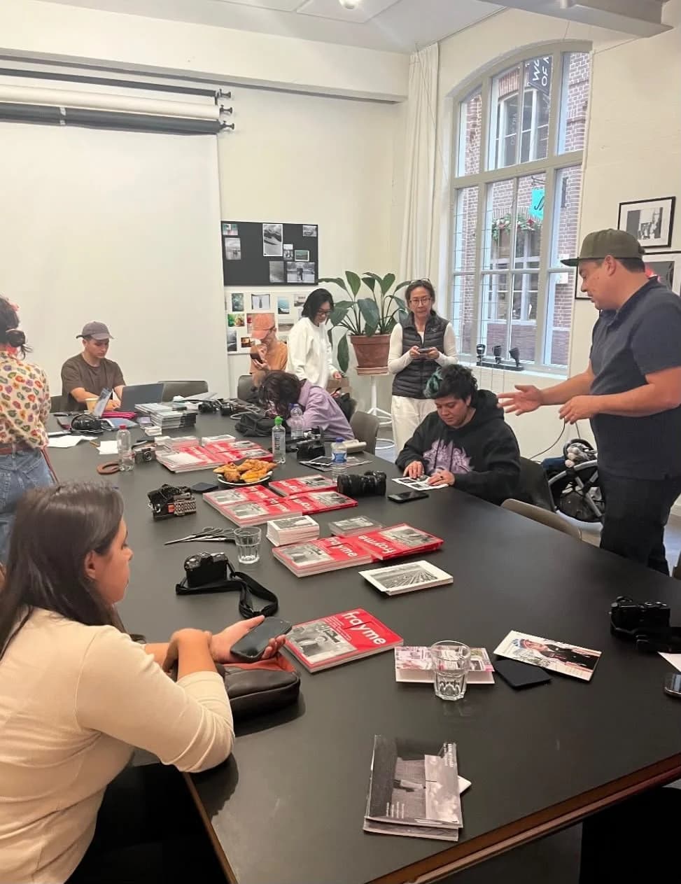 A zine workshop: photographers around a long table with laptops and prints